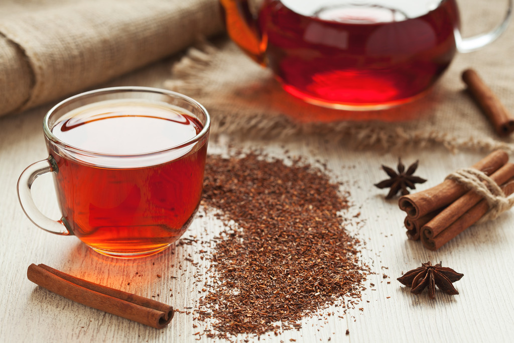 Traditional healthy red african rooibos tea in glass cup with spices on vintage table background